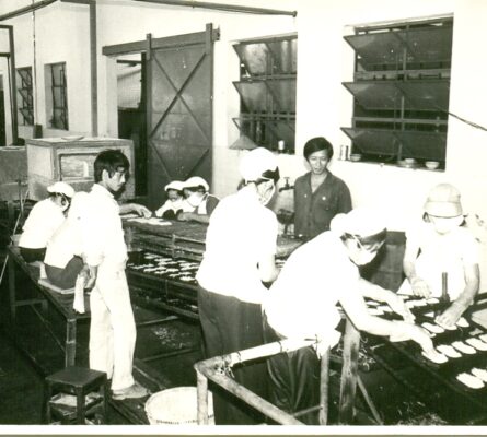 Black and white photo of people working in a food production facility, likely historical. Industrial food processing.